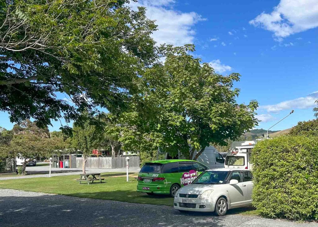 A car and campervans parked in grassy sites at the Alpine Pacific Holiday Park in Kaikoura, New Zealand.