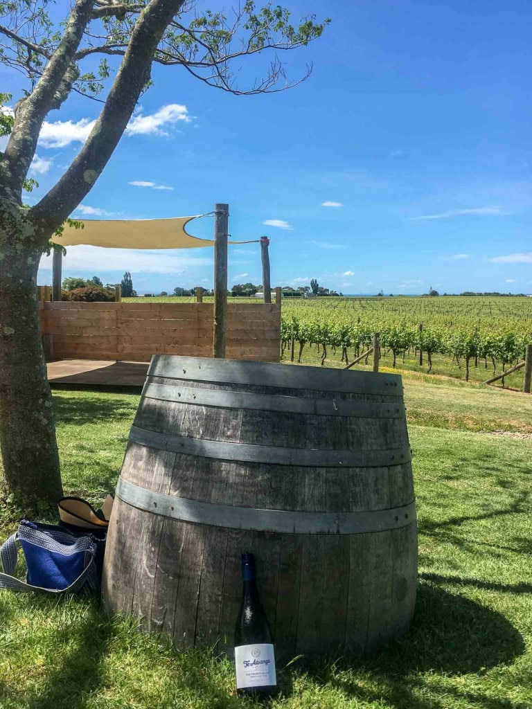 A wine bottle leaning against a wine barrel in front of a vineyard at Te Awanga Winery in Hawkes Bay.
