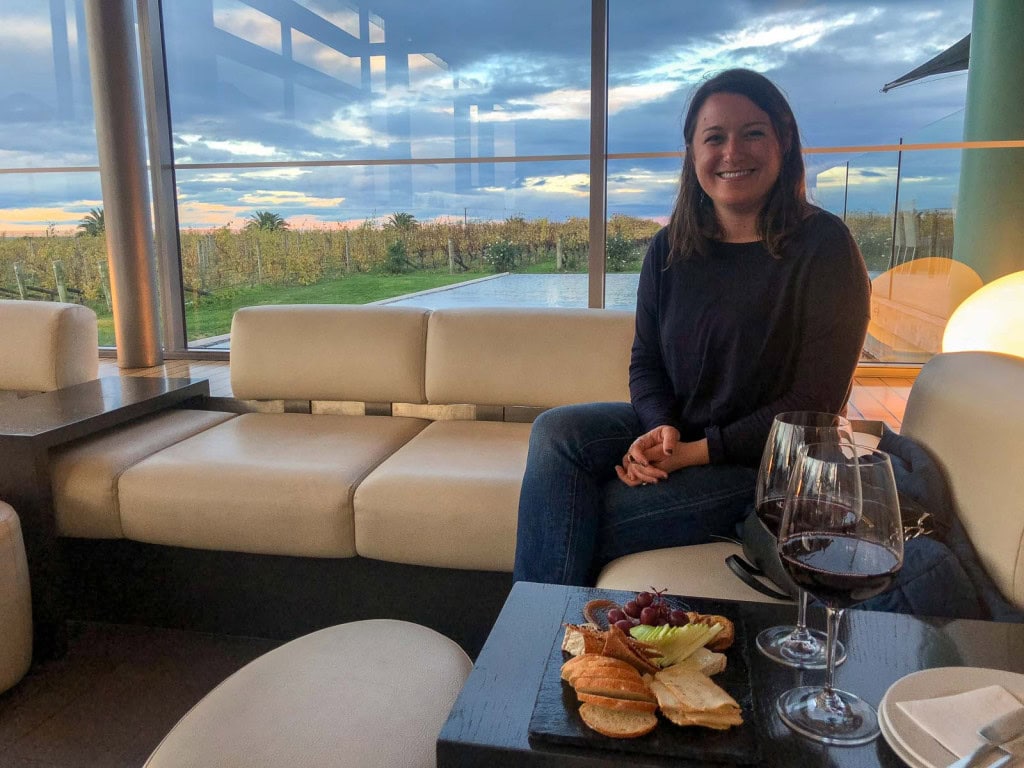 Jac from Weekend Path at Elephant Hill, a winery in Hawkes Bay, with red wine and a cheese board on a table and a view of the vineyard in the background.