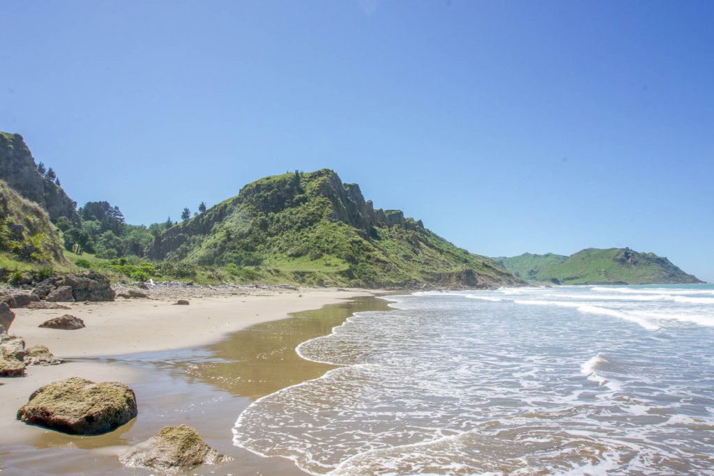 Kairakau Beach in Hawke's Bay, with a green headland at the northern end of the beach and a crescent of golden sand.