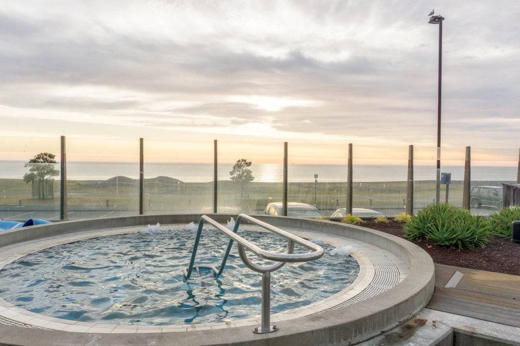 An outdoor hot tub with a view of the ocean at Ocean Spa, one of the best things to do in Napier on a cold day.